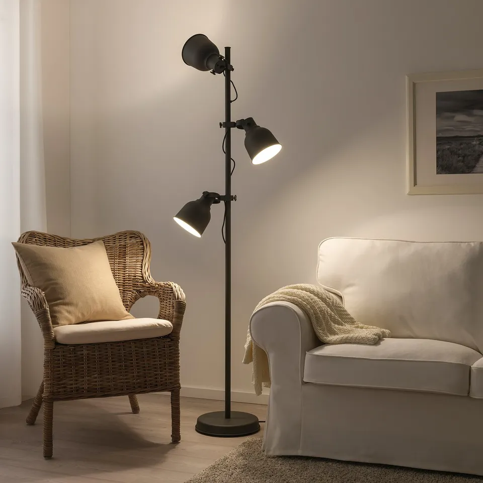 Two-headed black HEKTAR floor lamp between a beige wicker chair and an off-white couch, illuminating a calm living area.