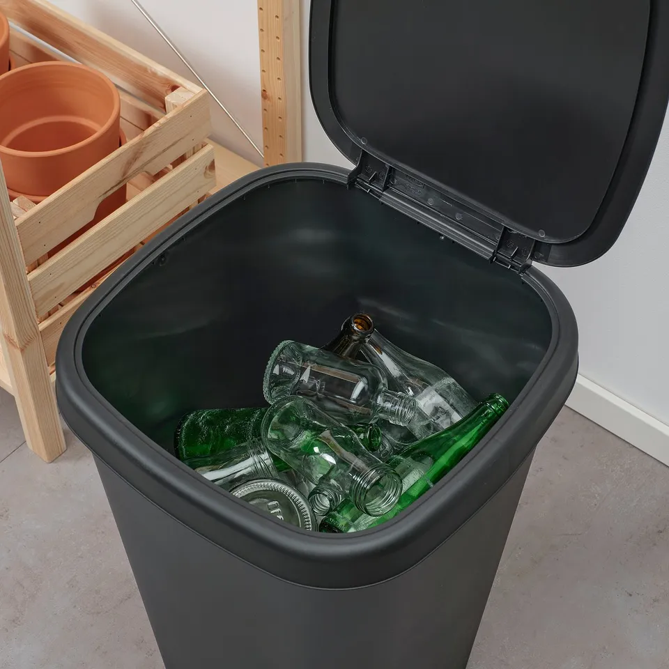 Black recycling bin with lid open, filled with various glass bottles.