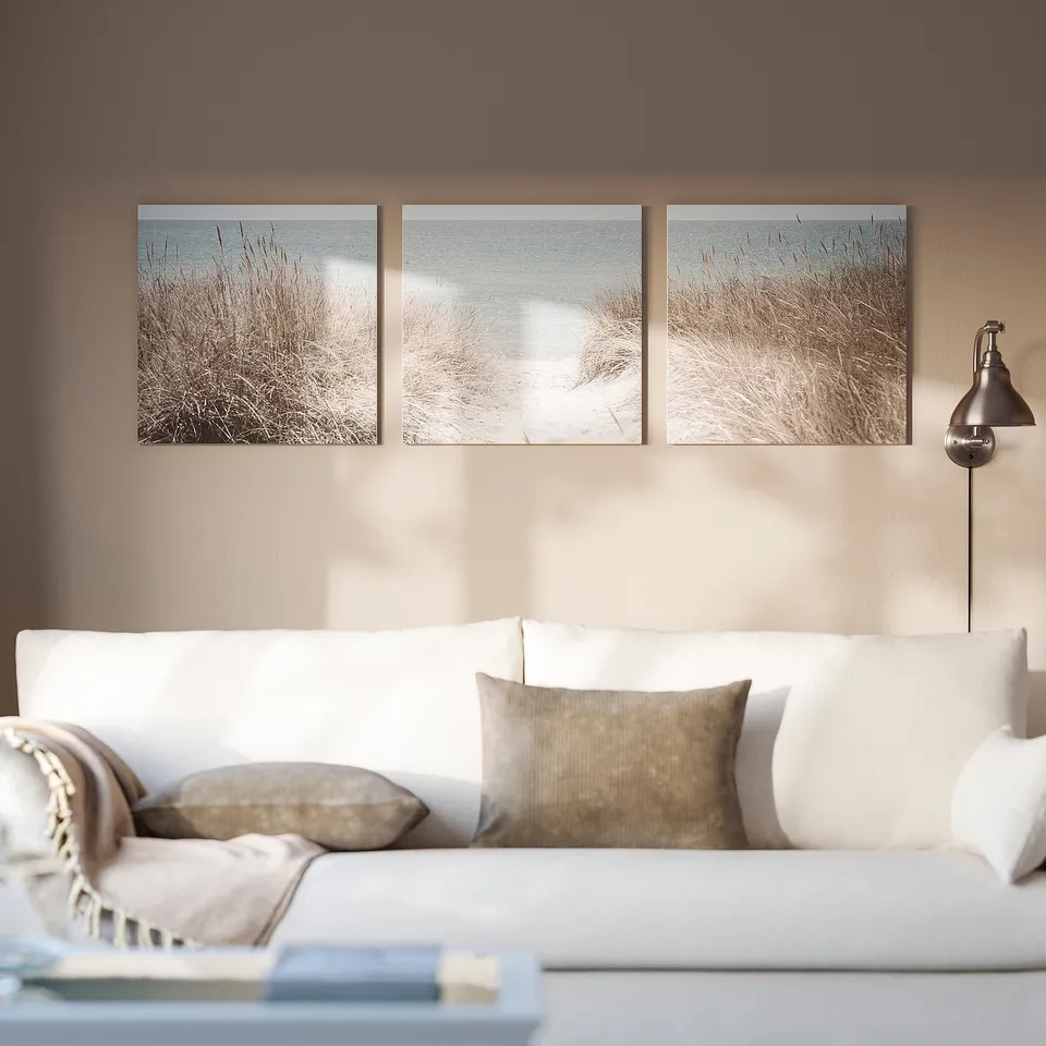 Light beach-themed art above white sofa, portraying dunes and ocean.