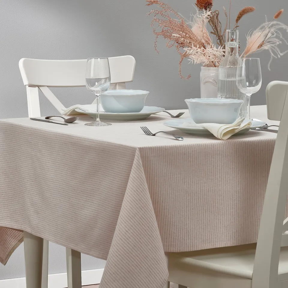 Table set with white chairs, a striped tablecloth, blue dishes, wine glasses, cutlery, and dried flower centrepiece.