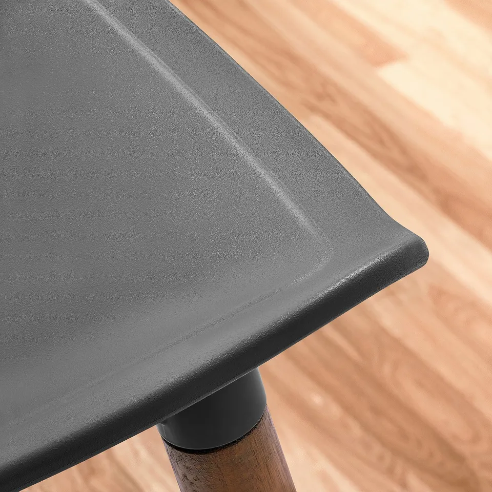 Modern black plastic chair seat on wooden floor, close-up view, smooth edges visible.