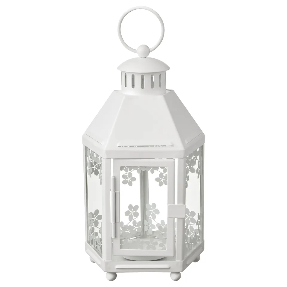 A white metal lantern with floral design, used indoors. Hexagonal shape, clear glass panels, and a hanging loop.