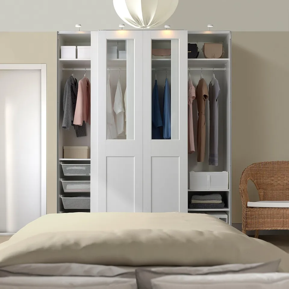 White PAX wardrobe with clothes, chair, and bed in neutral room.