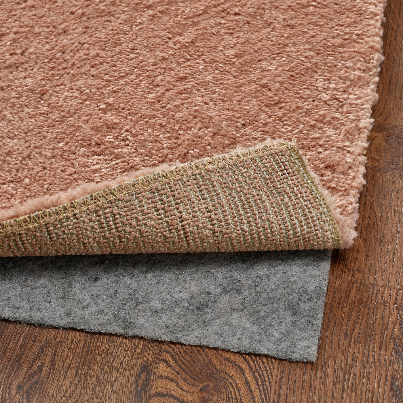 Soft pink rug with low pile, showing underside felt pad on wooden floor.