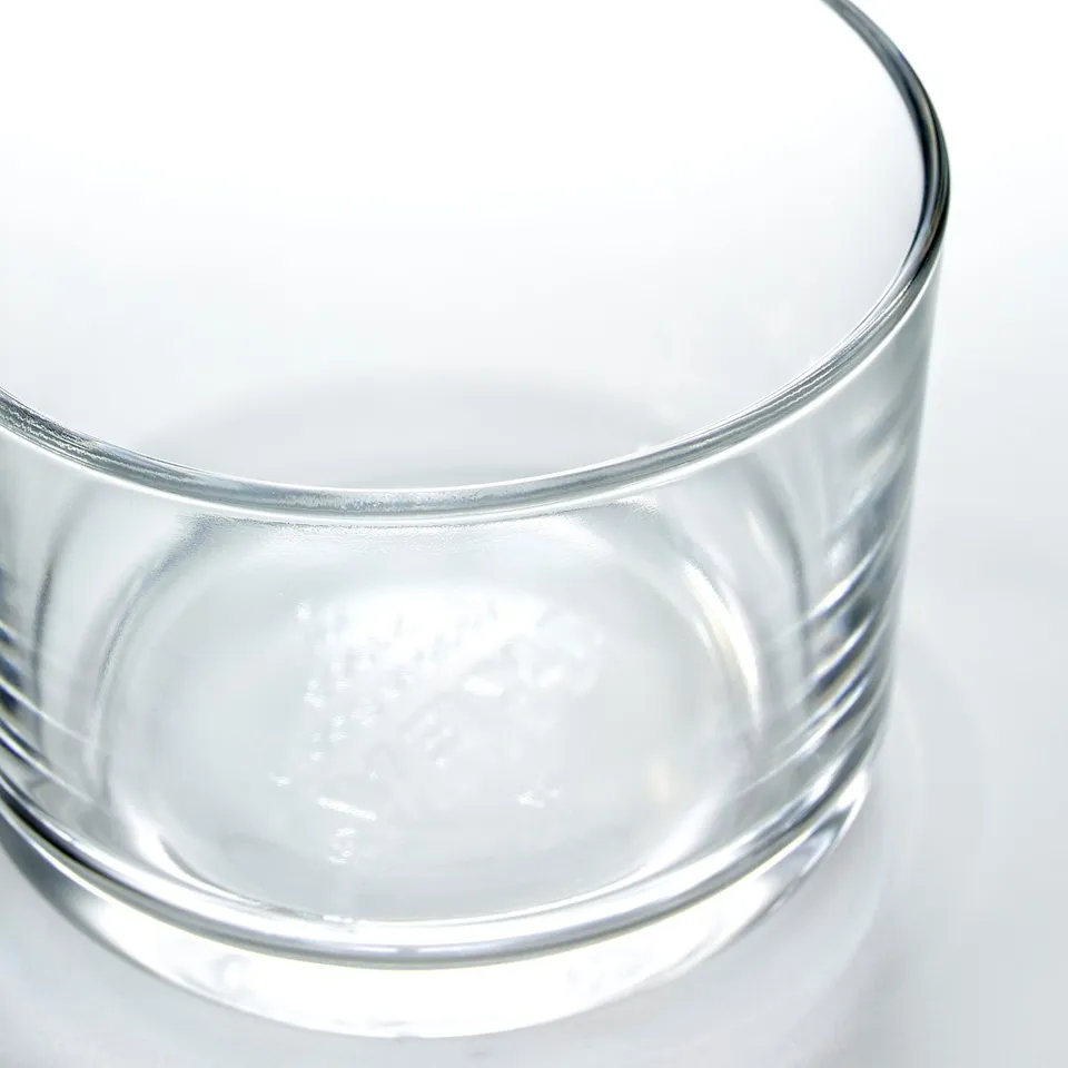 Clear, wide-mouthed glass on a white surface, reflecting light, showcasing its transparent and sturdy design.