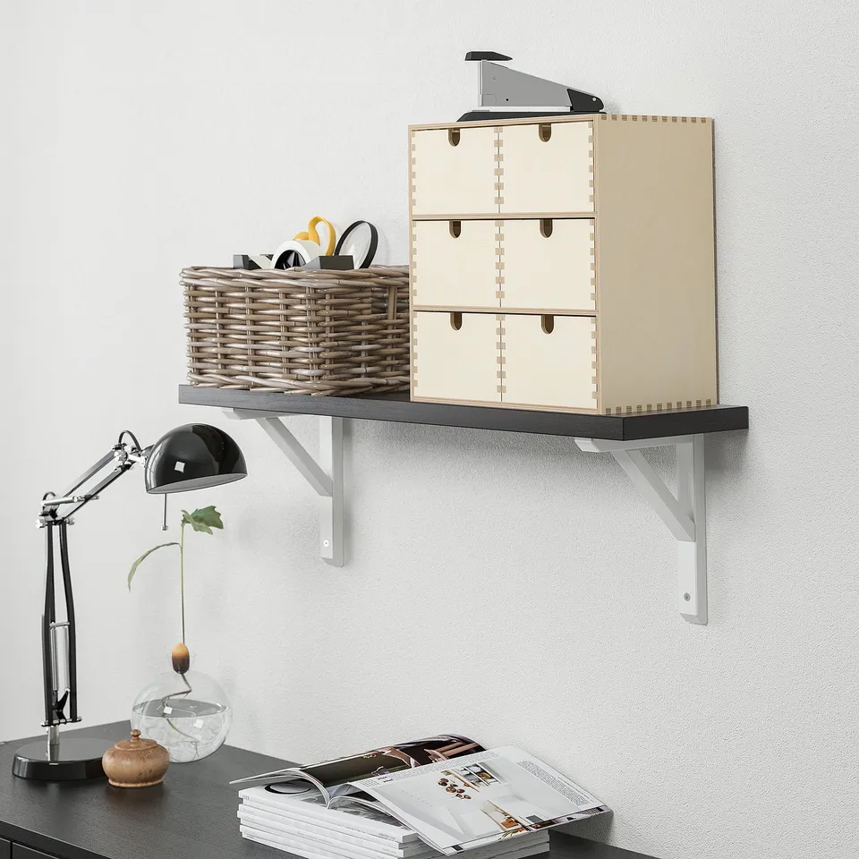Wall-mounted shelf holding wicker basket, wooden storage cubes, and stapler; supported by metal brackets. Below, desk with lamp and open magazine.
