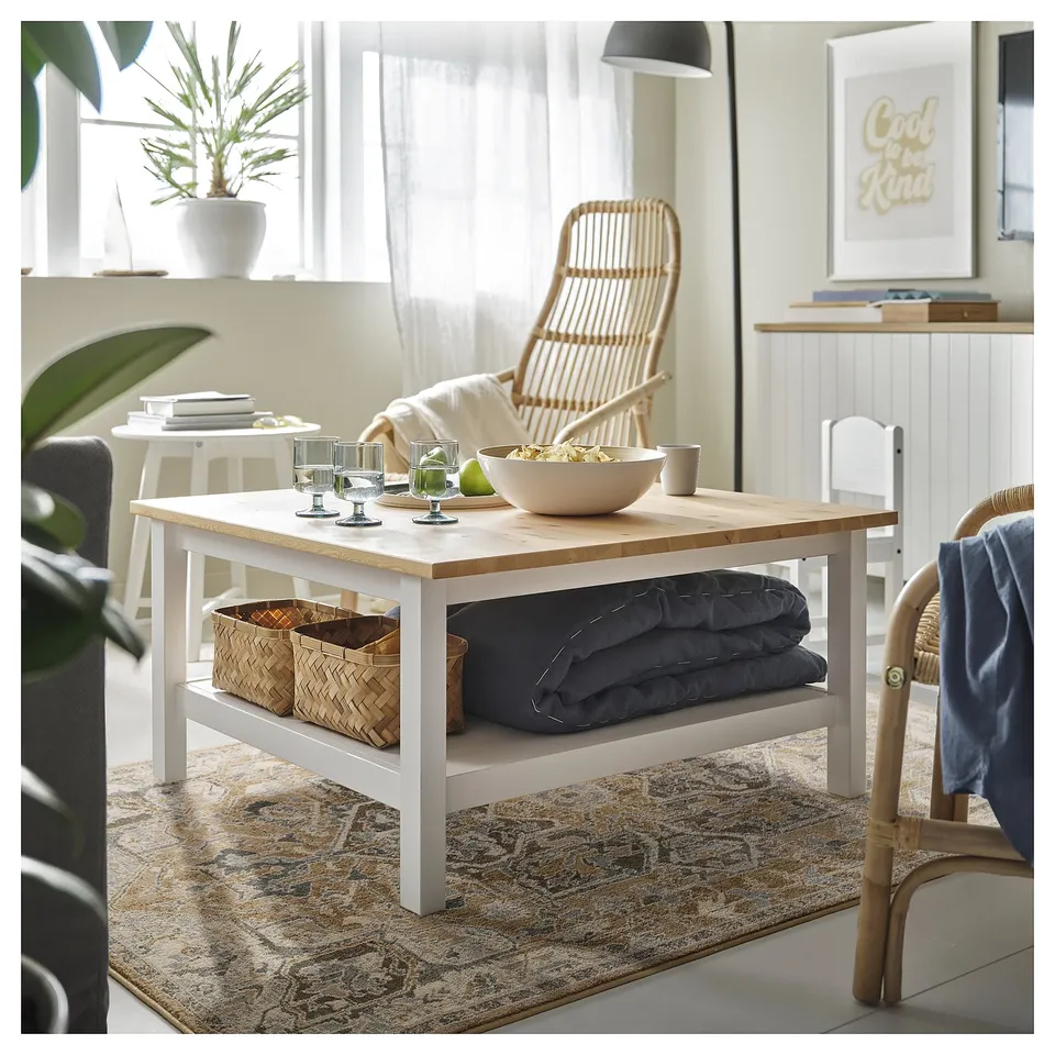 Modern living room with light brown JÄRNVÄG rug, white coffee table, and wicker chair with blankets and bowls on table.