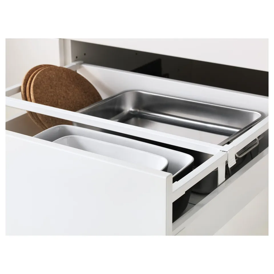 White kitchen drawer with two compartments: one for metal trays, one for plastic containers, and a cork trivet.