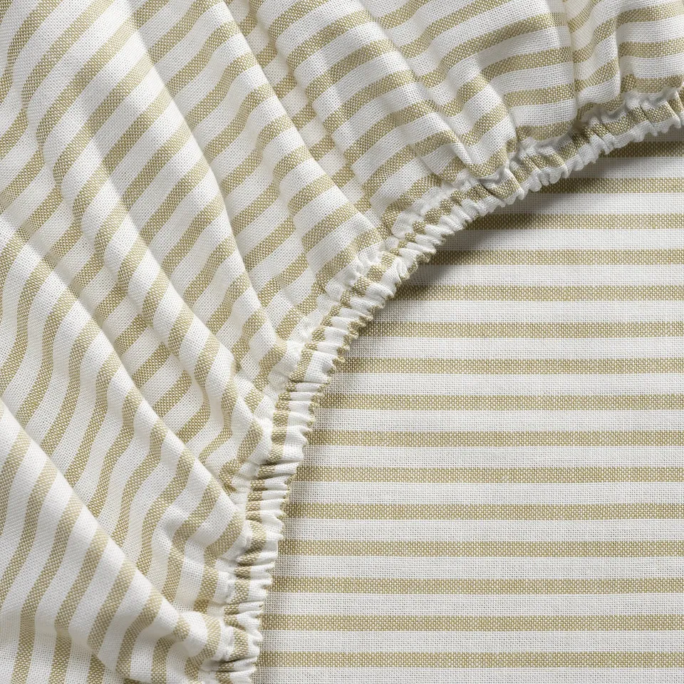 Beige striped bedsheet with ruffled edge, made of cotton, laid on a mattress.