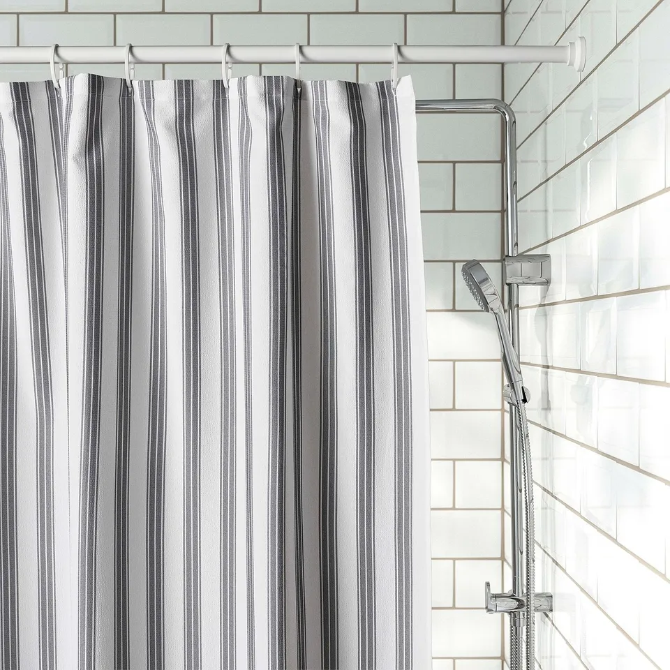 Striped shower curtain with vertical lines hangs from rod; water repellent and waves like soft fabric.