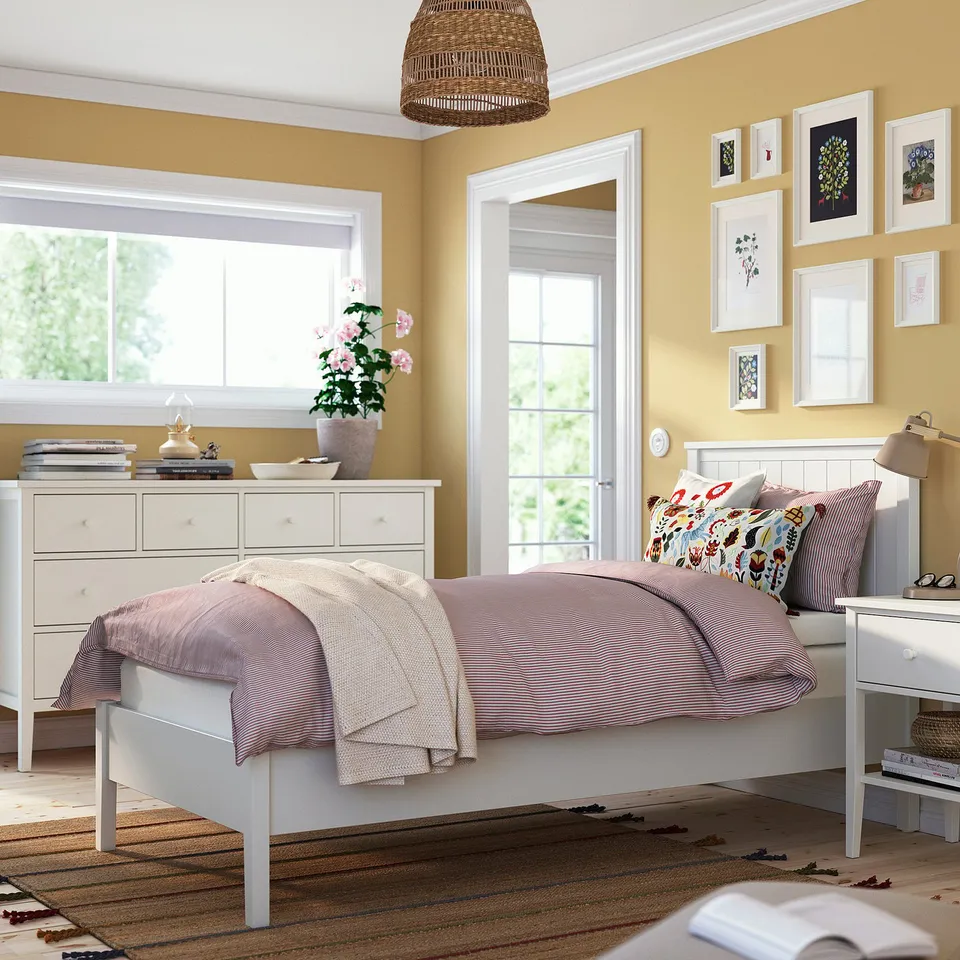 Cosy bedroom with GULLABERG bed, pink flowers, purple blanket, striped sheets, wall prints, and a tall chest of drawers.