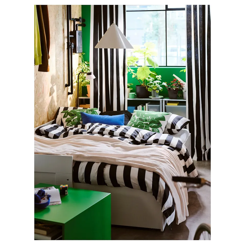 Bedroom with asymmetrical ZEBRASÄV recycled plastic pendant lamp over striped bed, surrounded by plants and green decor.