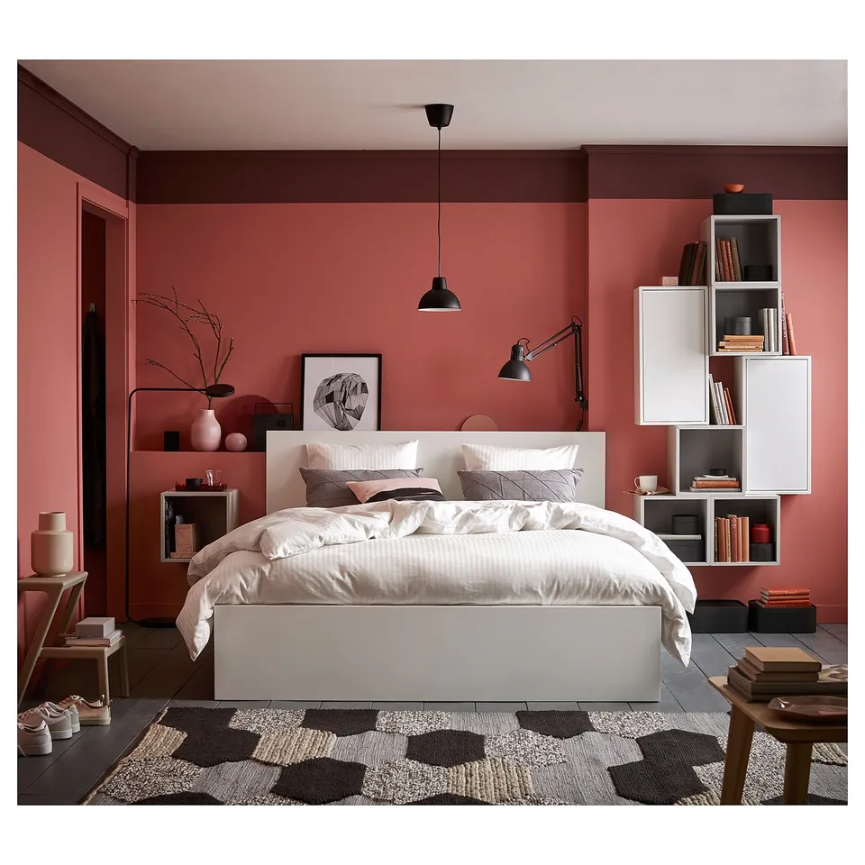 Modern bedroom with pink walls, white MALM bed, black pendant lamp, geometric rug, and wall shelves.