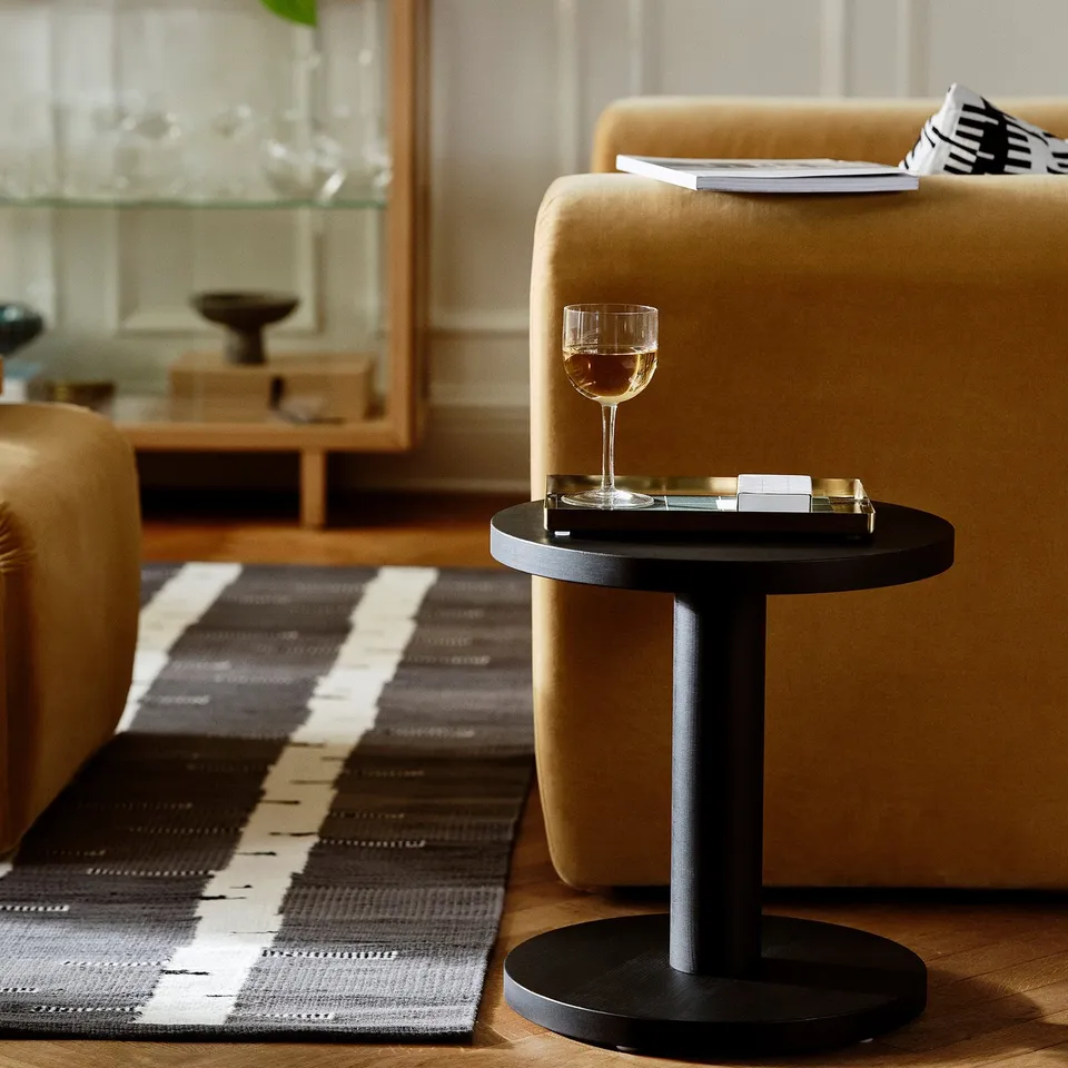 Grey wool rug with birch pattern near sofa, wine glass on side table.