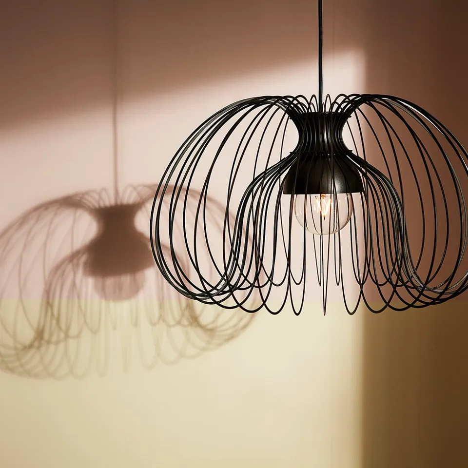 Two black, wireframe, pendant lamps hang from the ceiling, emitting light that casts intricate shadows on the wall.