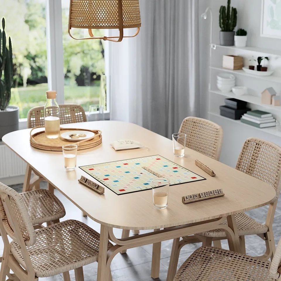 Light wooden dining table with wicker chairs, featuring a scrabble game board, glasses, and tray with snacks.