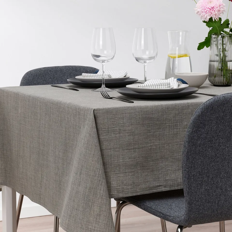 Table set with grey SVARTSENAP cloth, plates, glasses, cutlery, and vase. Seats 4-6.