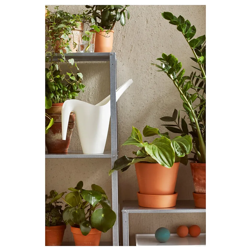 Modern metal plant shelf with clay pots and white vase.