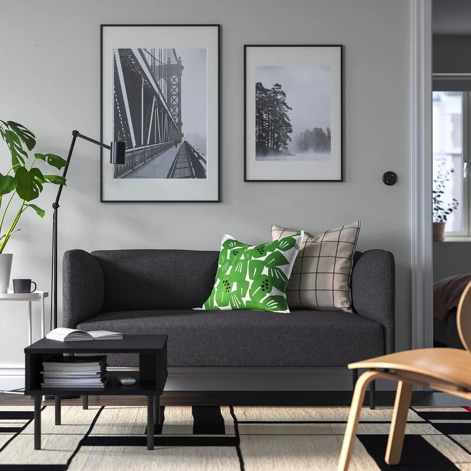 Grey LILLEHEM sofa with green pillows, wall photos, coffee table, books, mug, wooden chair, and plant.