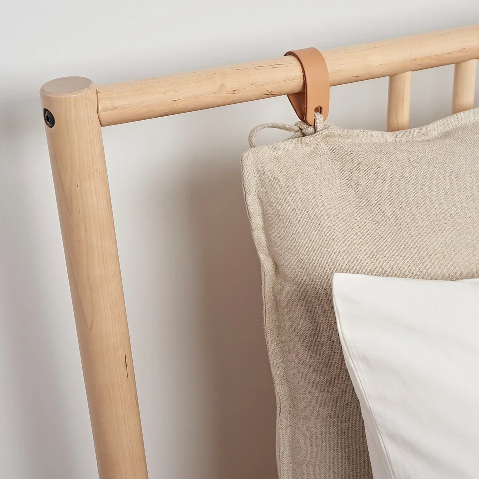 Light wooden bed frame with leather accents and beige linens. Quality craftsmanship with clean lines and natural materials.