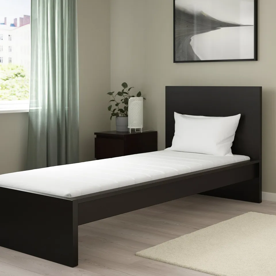 Black foam mattress in bedroom with green walls. Medium-firm, 12 cm thick, with pillow and bedside table.