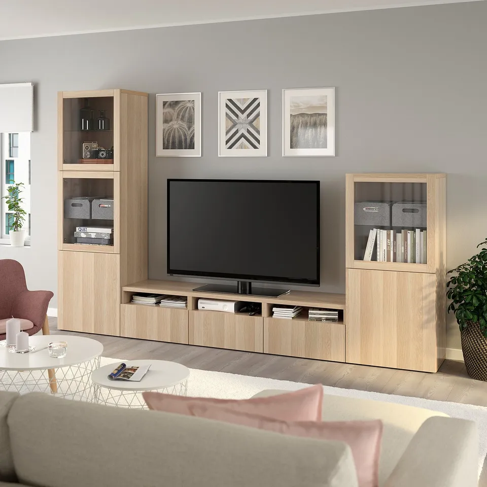 Modern living room with BESTÅ tv unit, flat-screen tv, decor, white couch, pink accent chair, and coffee table with magazines.