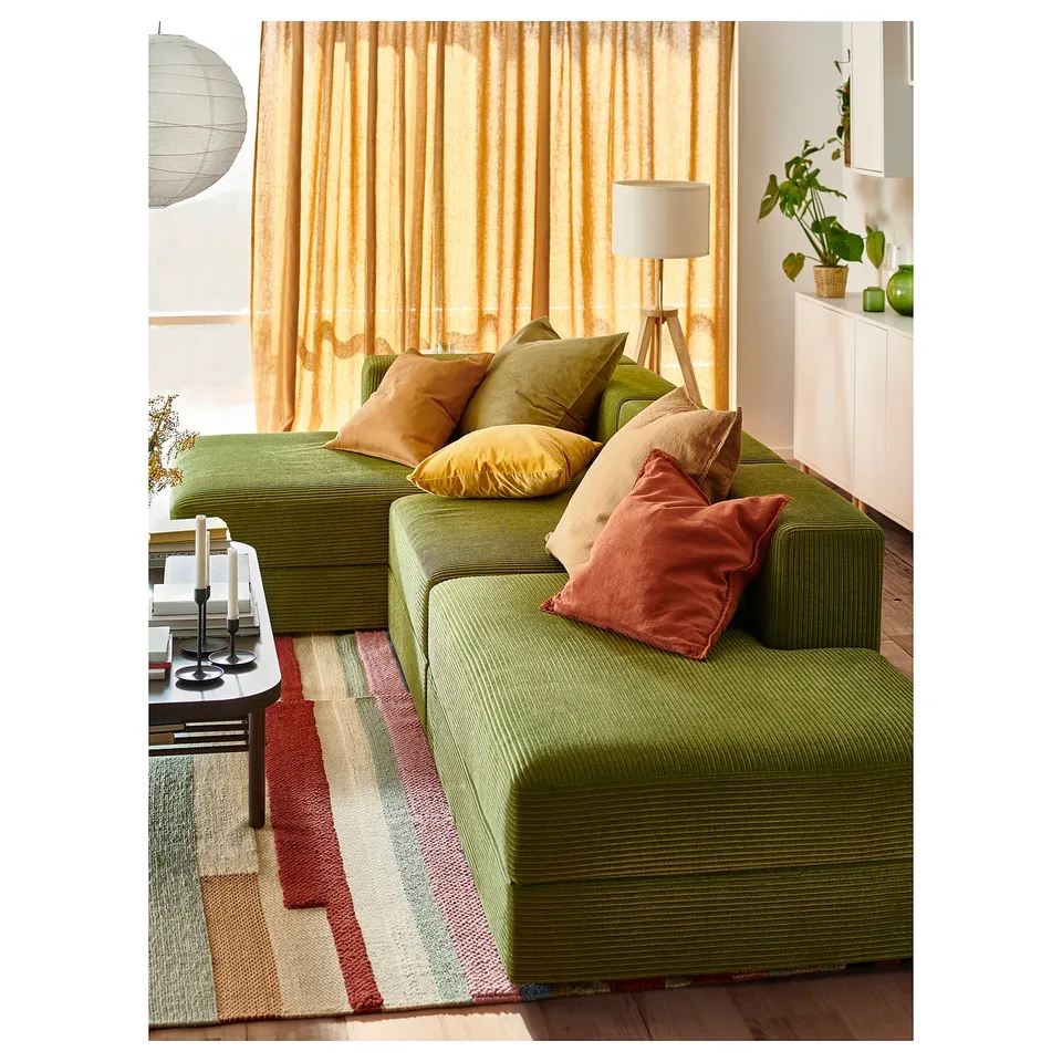 Green modular sofa with orange pillows, rug, and floor lamp.