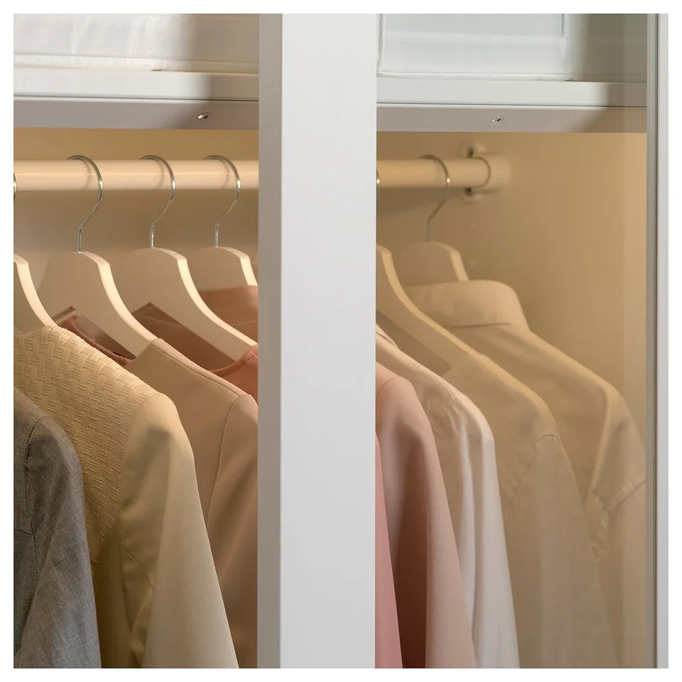 A PAX wardrobe with white sliding doors. Clothes hangers with beige clothes are visible through the glass panel.
