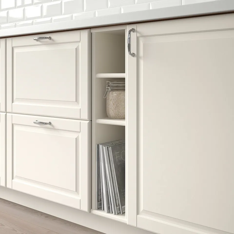 White kitchen cabinet partially open, revealing books and a decorative jar.