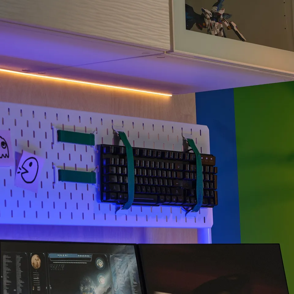 Led strip under shelf, illuminating keyboard on pegboard with rgb lights. Desk with monitor below, colourful walls.