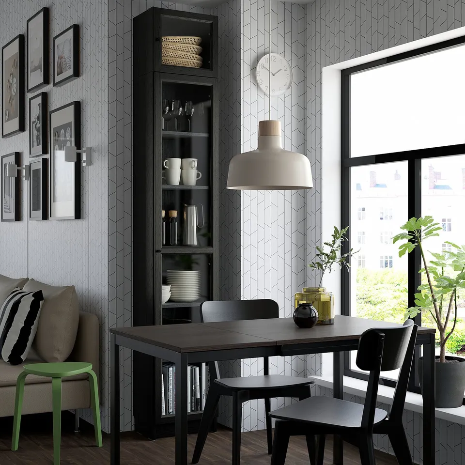 Modern dining area with glass-door bookcase, dishes, clock, black chairs, green stool, garden view.