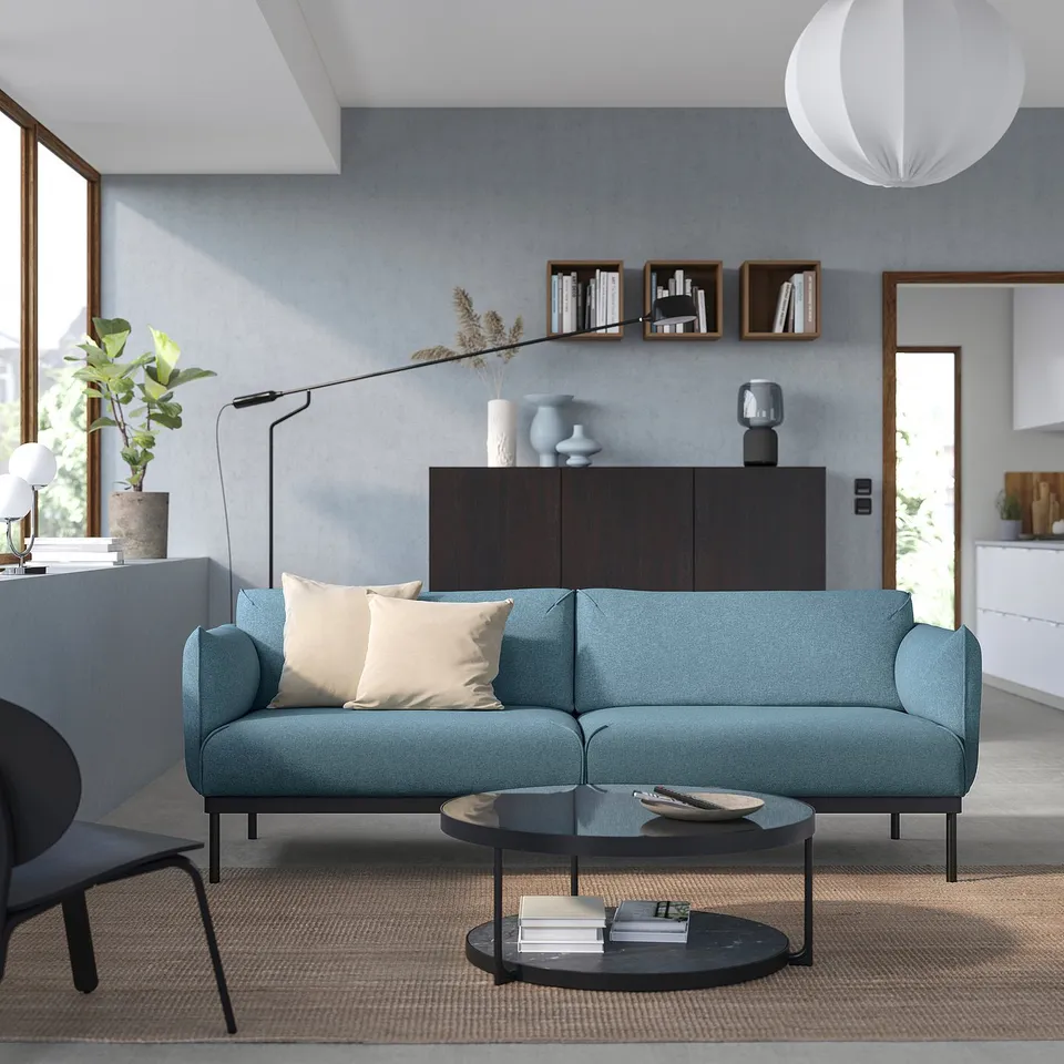 Modern living room a blue ÄPPLARYD sofa with beige cushions, round coffee table, and sleek decor.