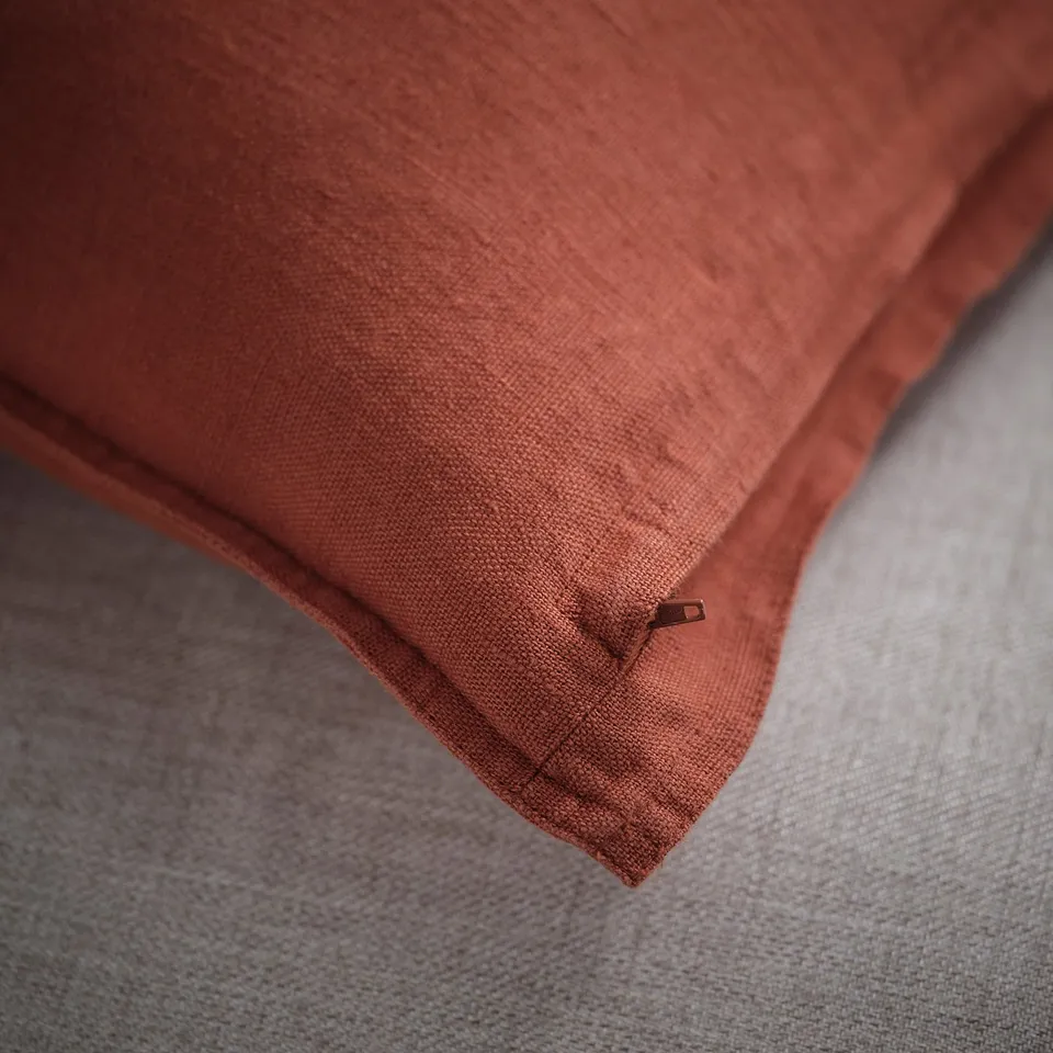 Close-up of rust-colored cushion cover with visible zip, showcasing soft texture and fine weave of washed linen.