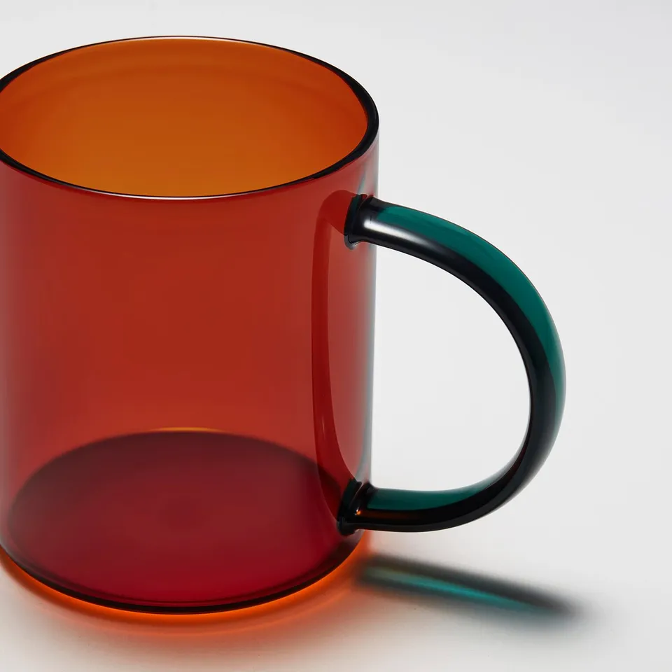 Bright red transparent glass mug with sturdy black handle. Sunlight casts clear shadow.