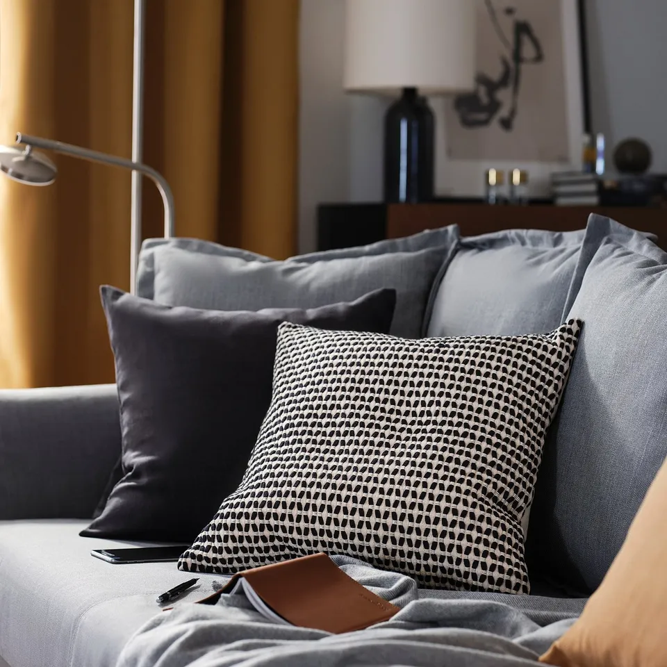 Modern living room with grey couch, black & patterned pillows, phone, and wallet.