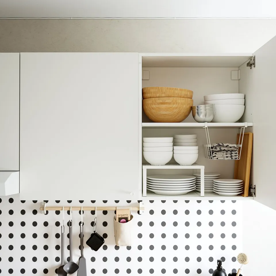 Kitchen wall cabinet with adjustable shelves holding bowls, plates, and cups. Polka-dot backsplash and hanging utensils.