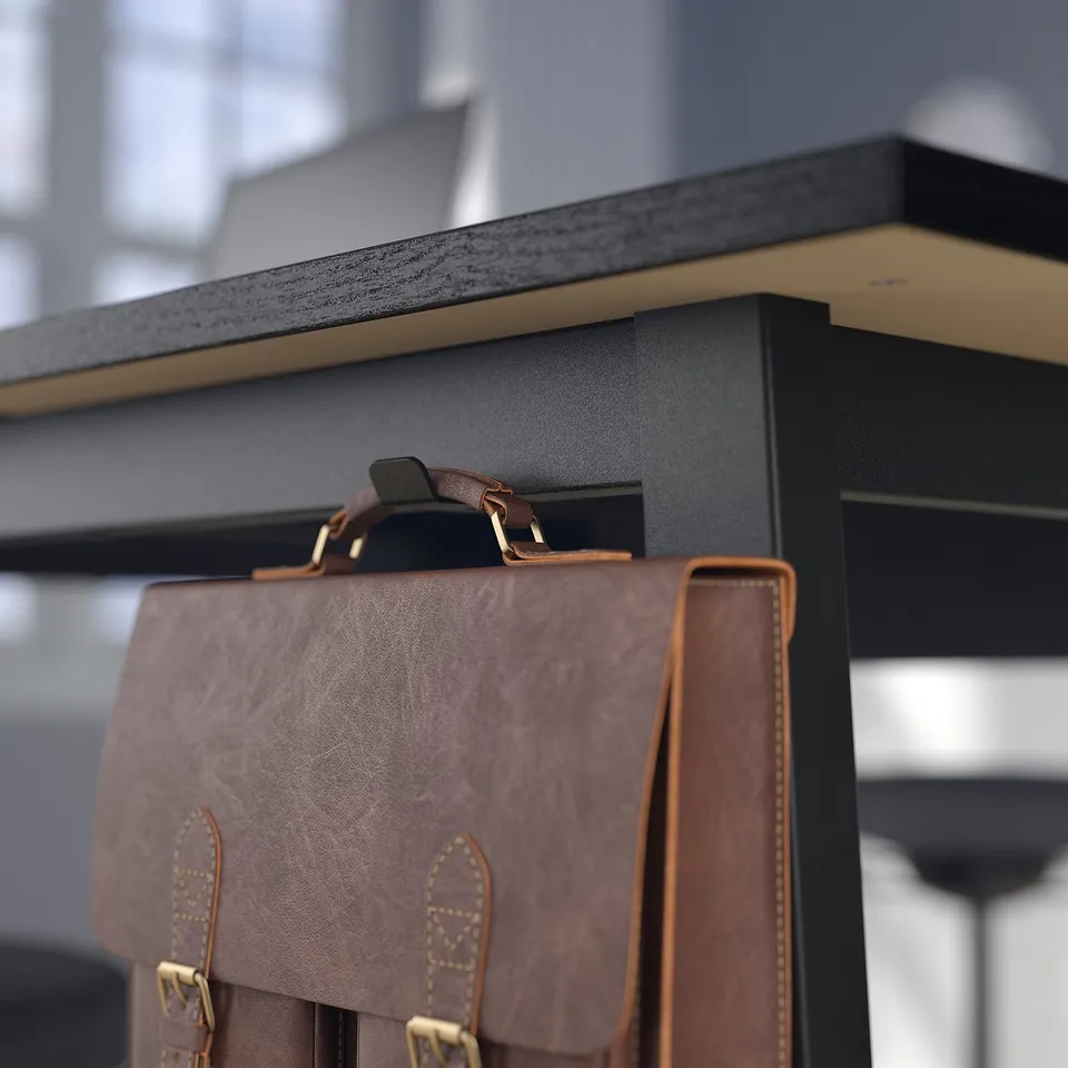 Leather bag hangs from black desk with footrest and cable management module.