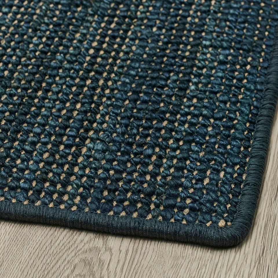 Dark blue jute rug on light wooden floor, folded corner, showcasing dense, woven texture, natural latex backing visible at edge.