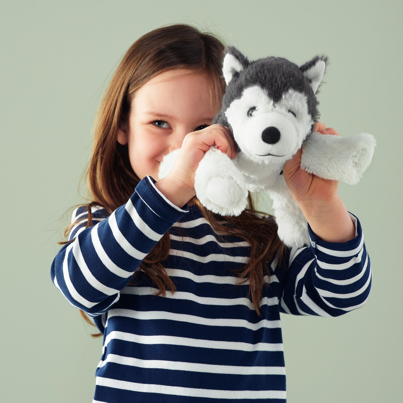 Girl with blue sweater hugging plush husky toy.