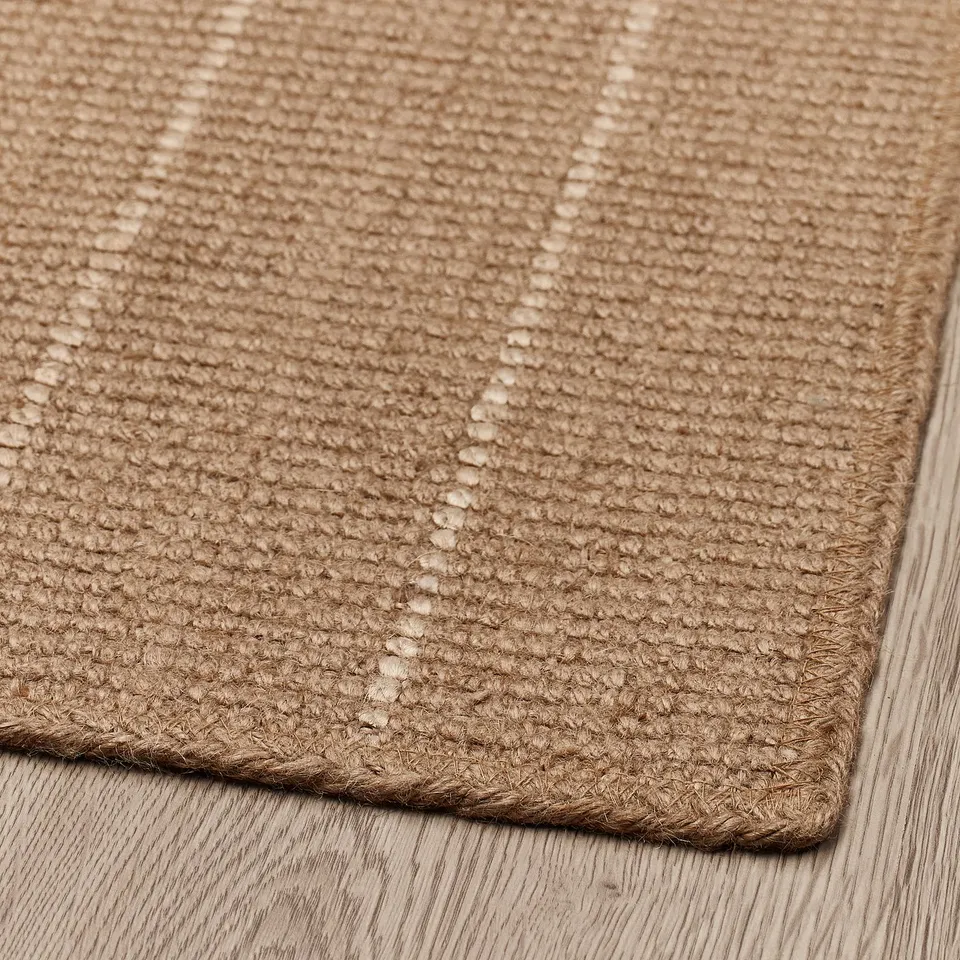 Close-up of woven jute door mat on wooden floor. Natural texture, braided edges visible.