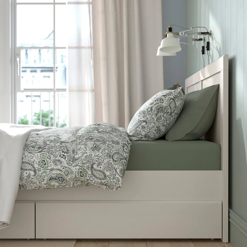 Bed with white headboard and storage drawers, green bedding, and wall lamp.