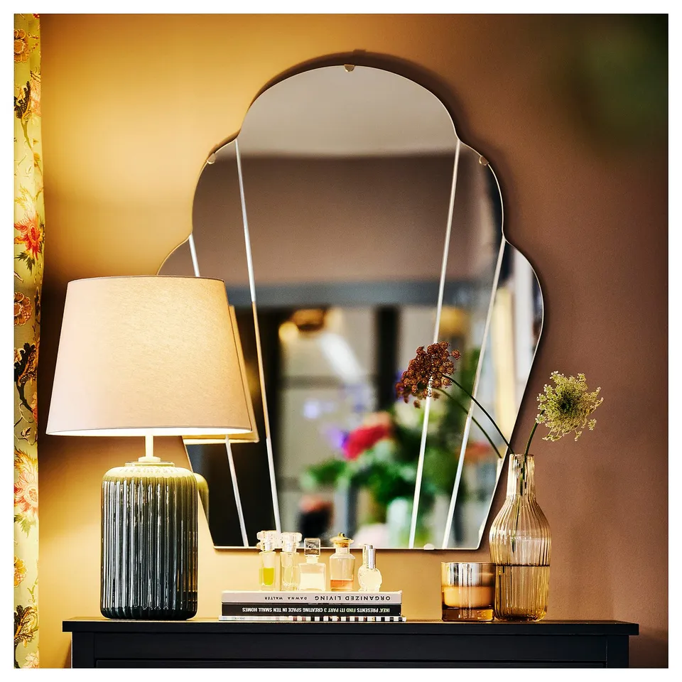 Neat vanity setup: black lamp, white shade; triangular mirror; perfume bottles; dried flowers.
