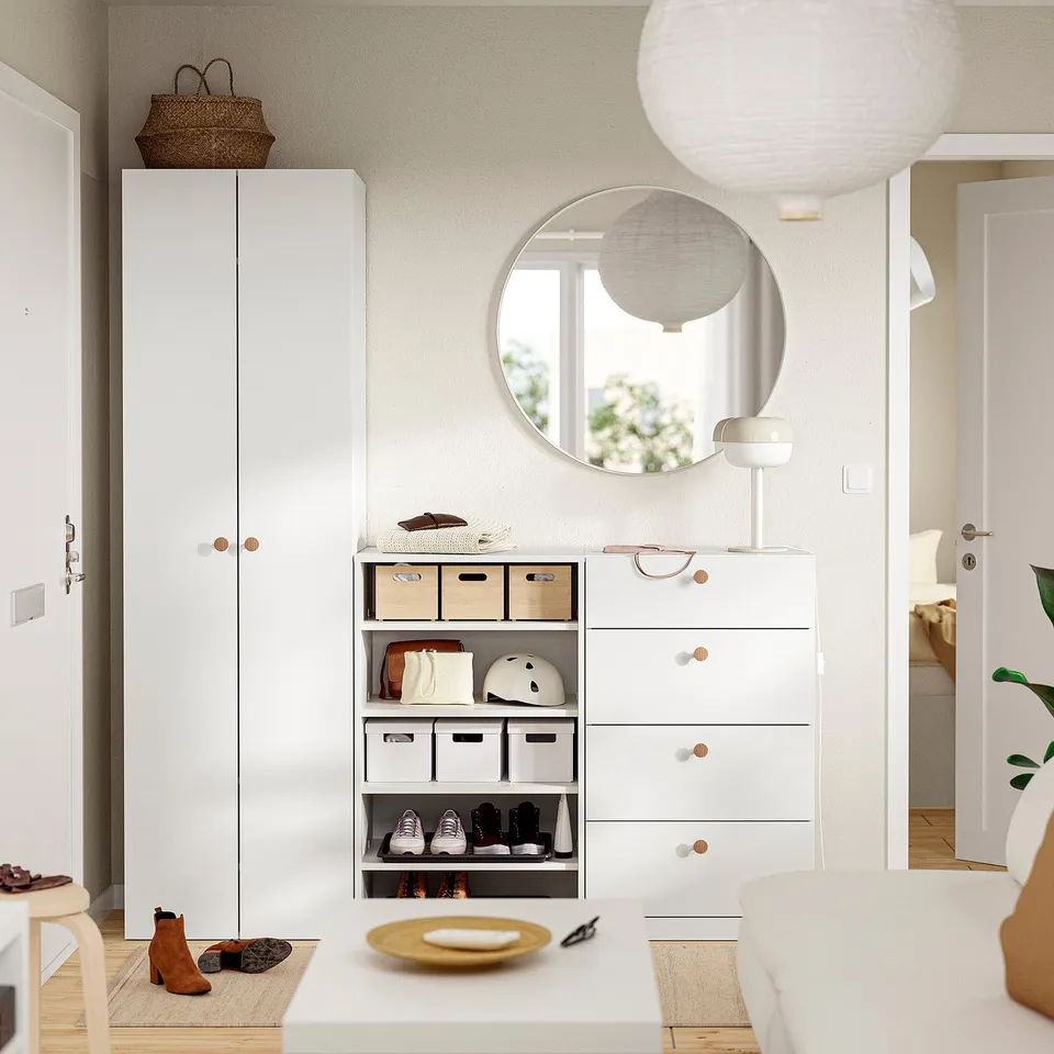 White entryway with cabinet, drawers, mirror, lamp, shoes, bags.