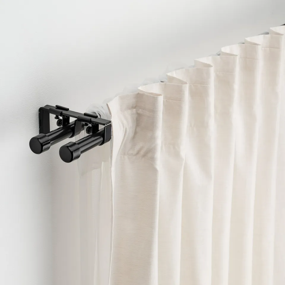 Black curtain rod set with white curtains, holding them neatly against a light wall.