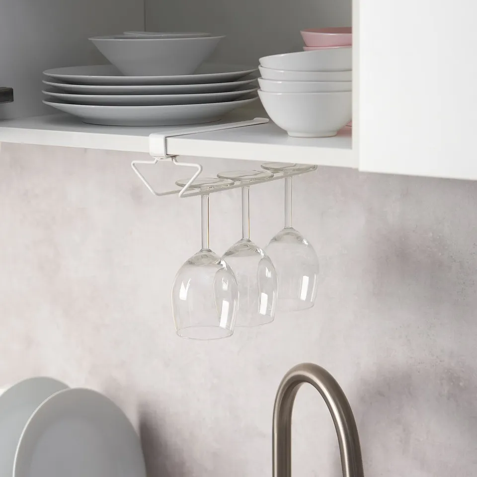A PÅLYCKE wine glass rack mounted under a white shelf, holding four wine glasses and keeping them safely out of the way.
