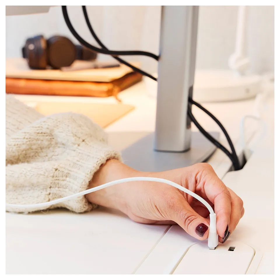 Hand adjusts white MITTZON desk height button, beige sweater visible, wooden desk surface behind.