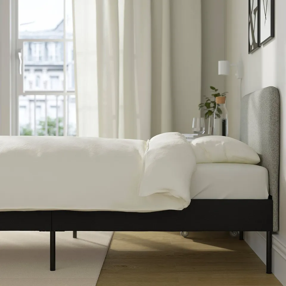 Bedroom scene with modern SLATTUM bed. Upholstered headboard, clean lines, and wooden floor.