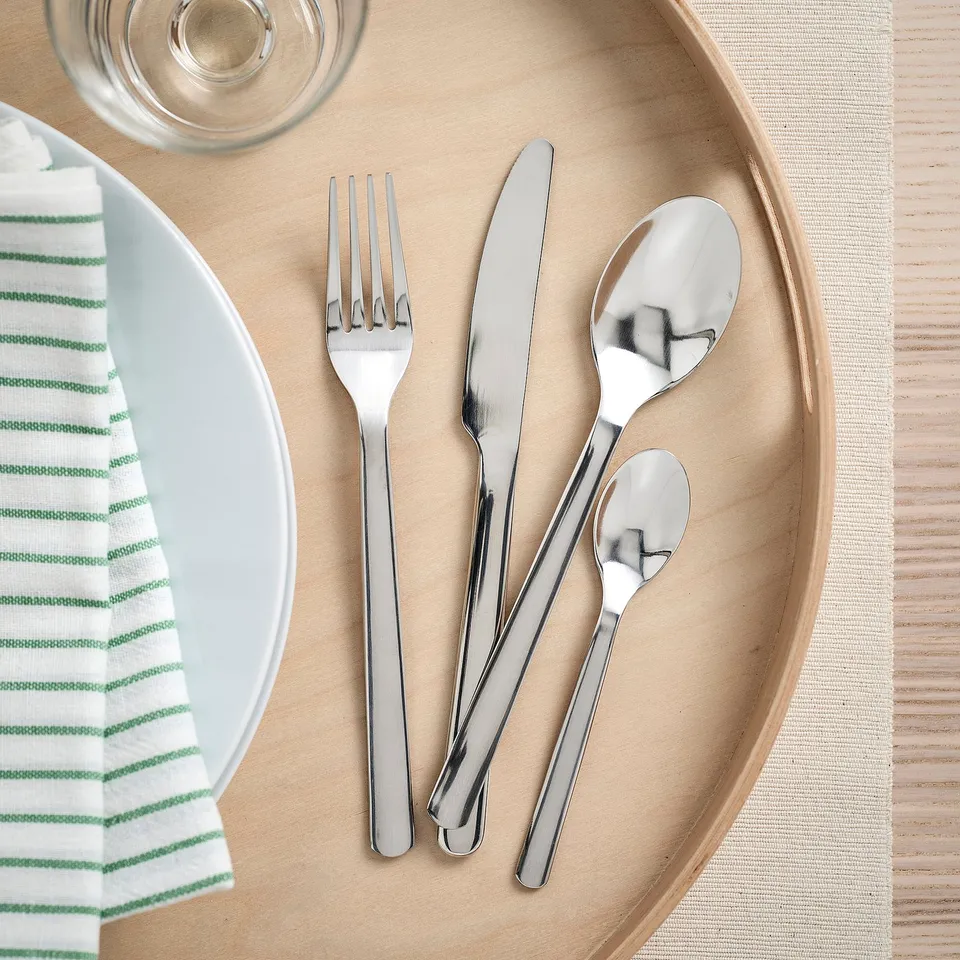 Stainless steel IKEA 365+ cutlery set: fork, knife, spoons on plate with napkin, glass, placemat.