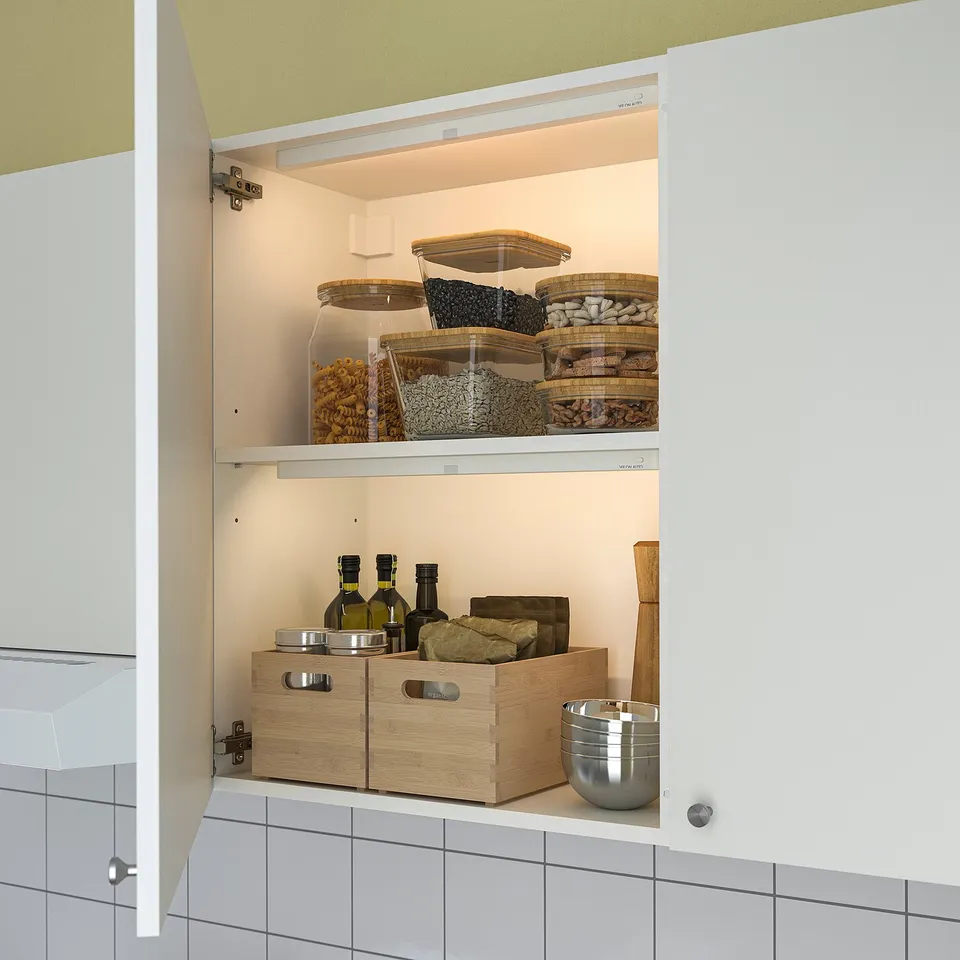 Open kitchen cabinet with lit KÖLVATTEN light strip, showing organised food items and boxes.