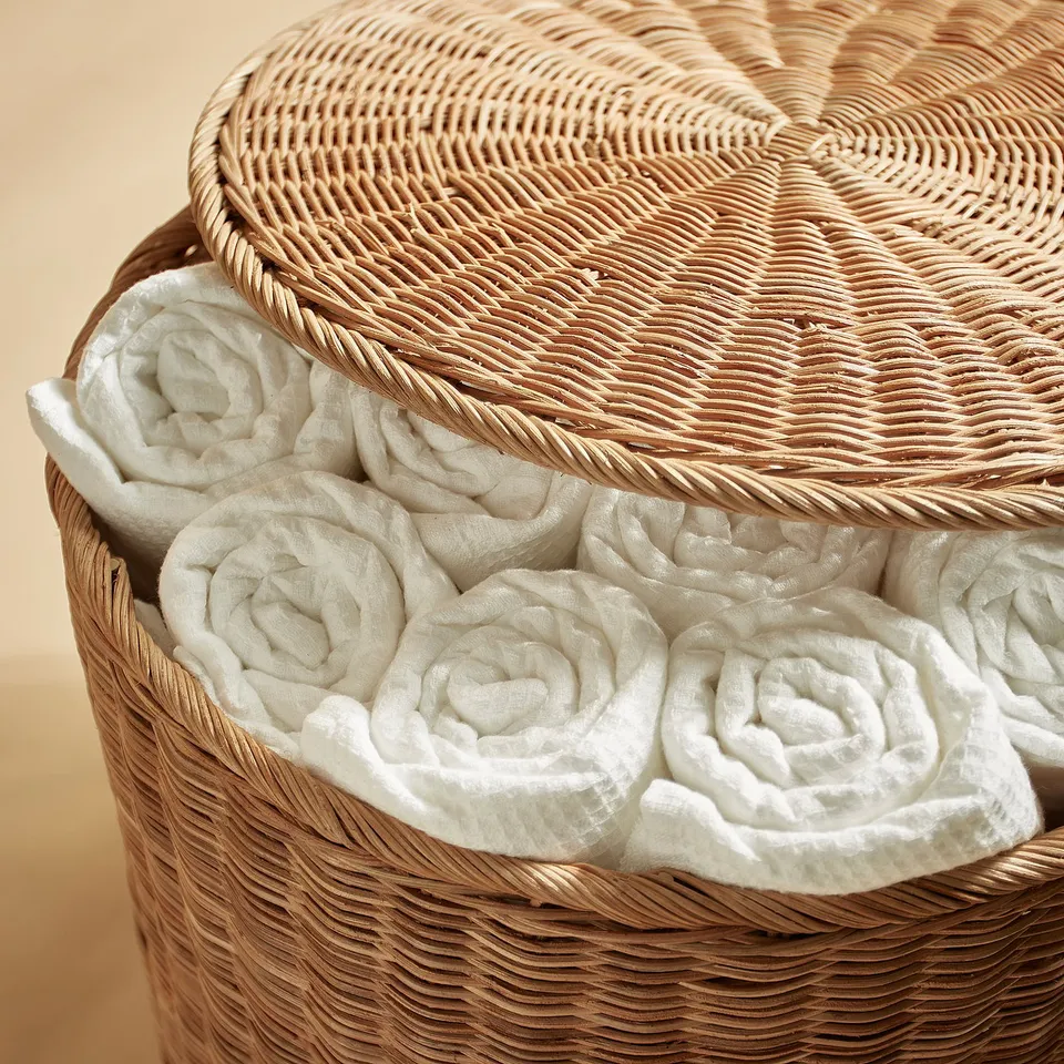 Round woven rattan basket filled with neatly rolled white towels, showcasing quality craftsmanship and storage.